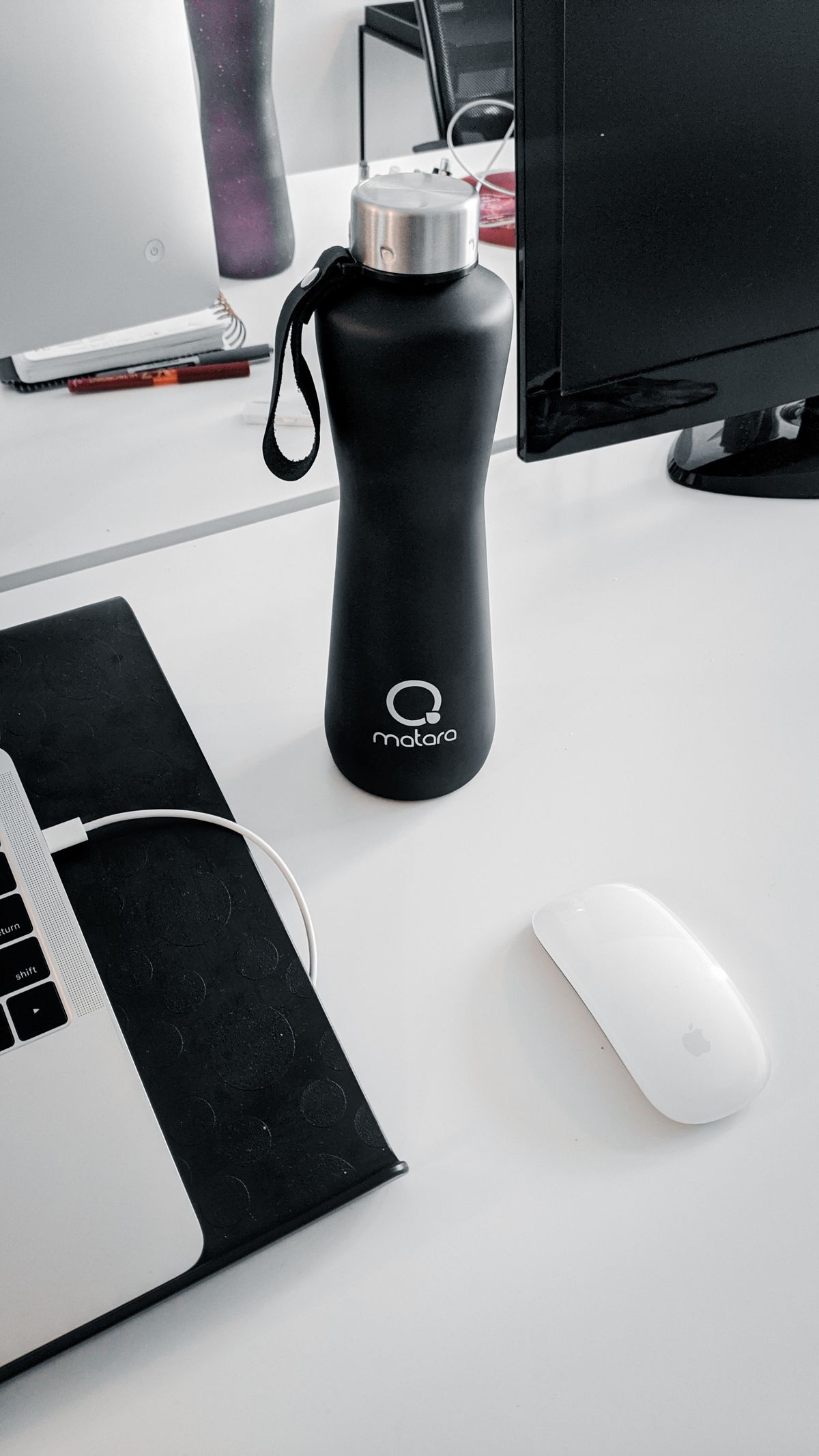 Botol minum hitam berdiri di meja dekat monitor, laptop, dan mouse.