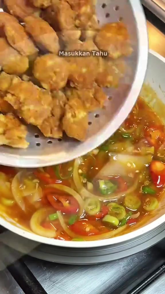 Potongan tahu goreng dimasukkan ke dalam saus yang sedang dimasak