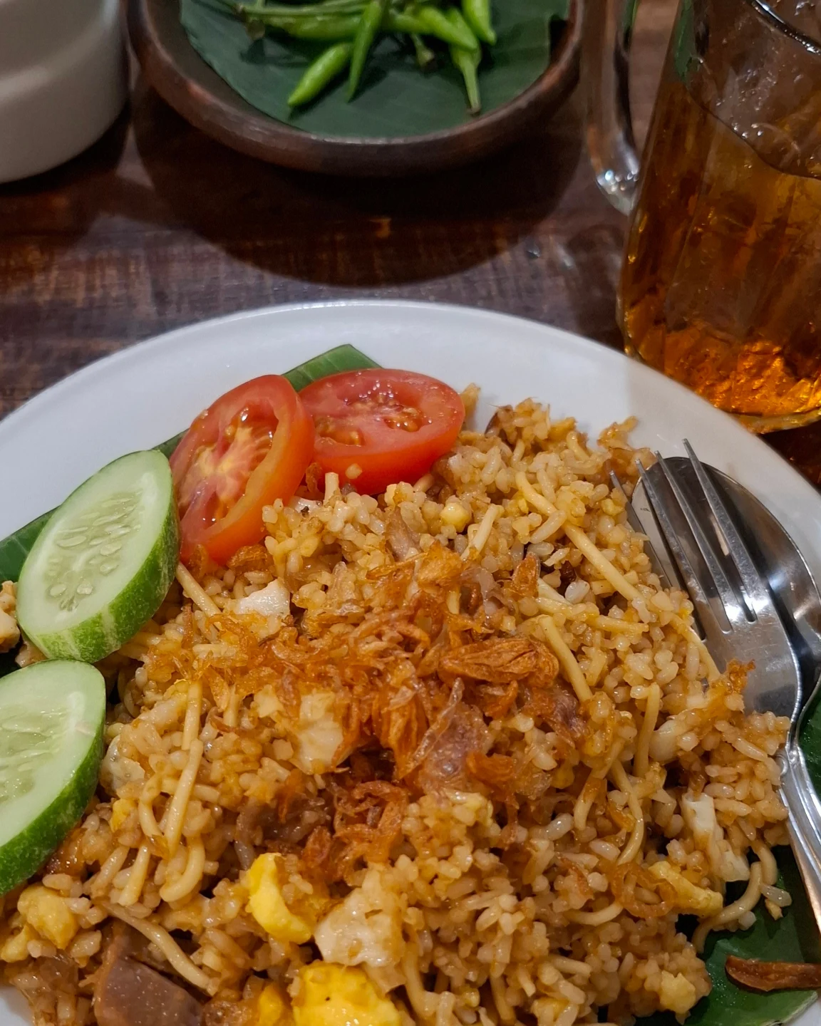 Nasi goreng mawut campur mie dengan bawang goreng, irisan tomat dan timun di piring putih