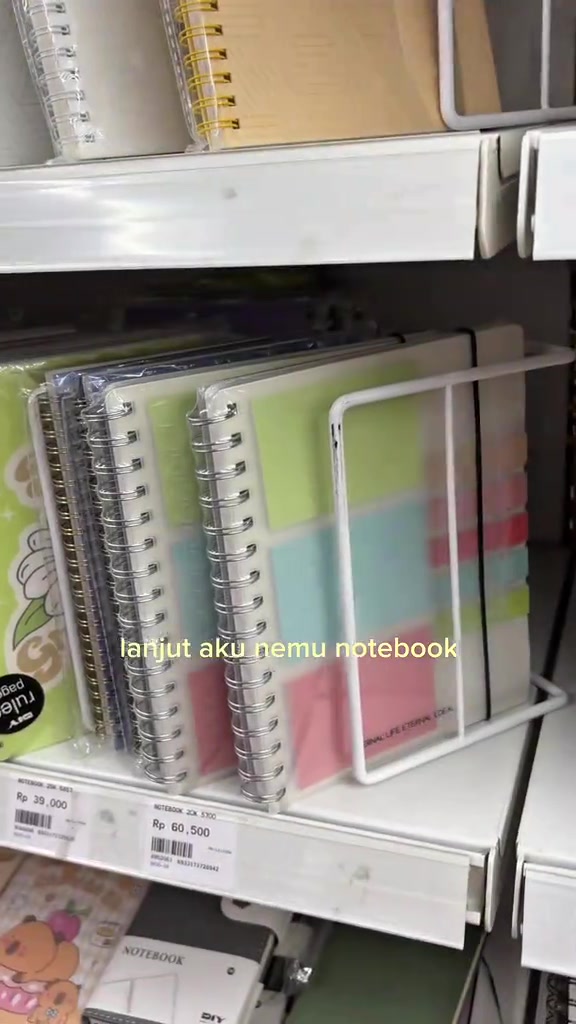 Deretan notebook spiral warna pastel di rak alat tulis