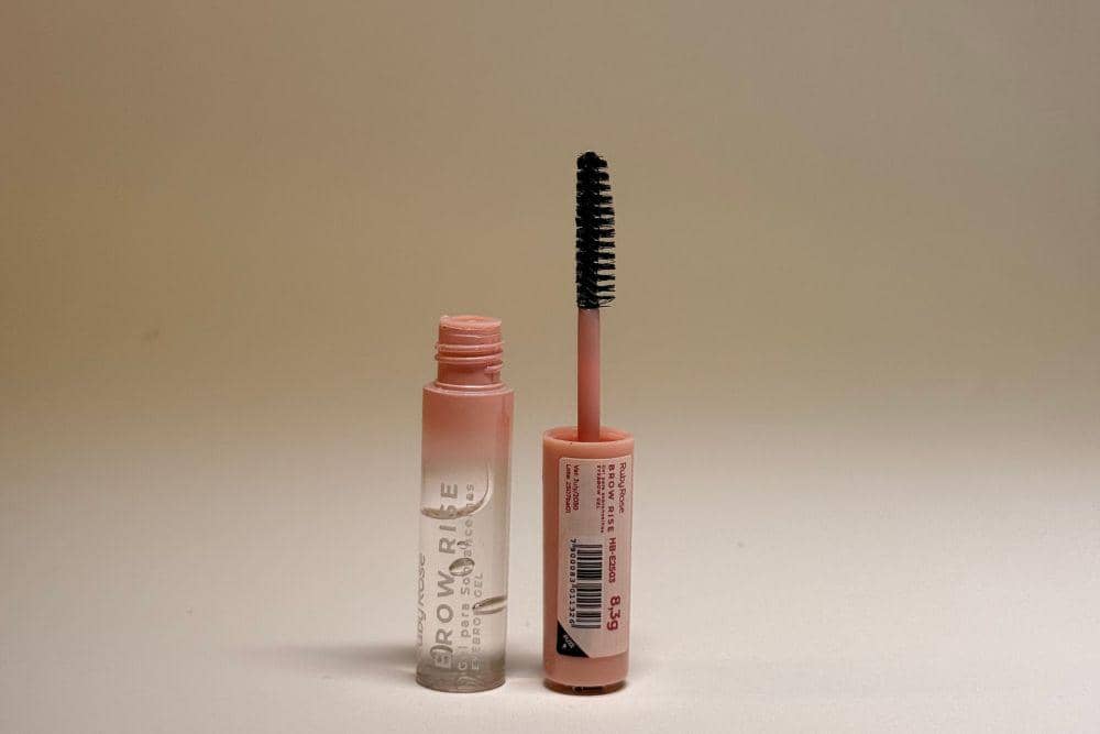Tube browcara warna peach dalam keadaan terbuka dengan aplikator spoolie mini berdiri di sampingnya