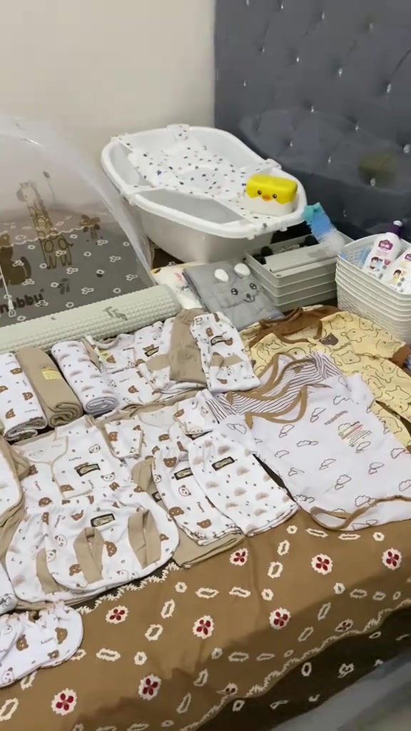 Pakaian bayi, kain, dan bak mandi kecil tertata di atas alas bermotif