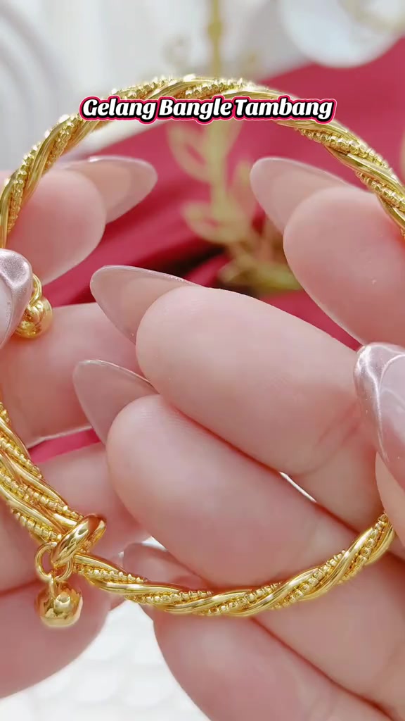 Gelang bangle gold motif tambang dipilin dipegang ujung jari dengan latar merah muda