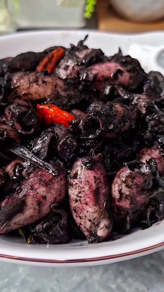 Cumi masak tinta hitam yang mengilap dengan cabai rawit merah di piring putih
