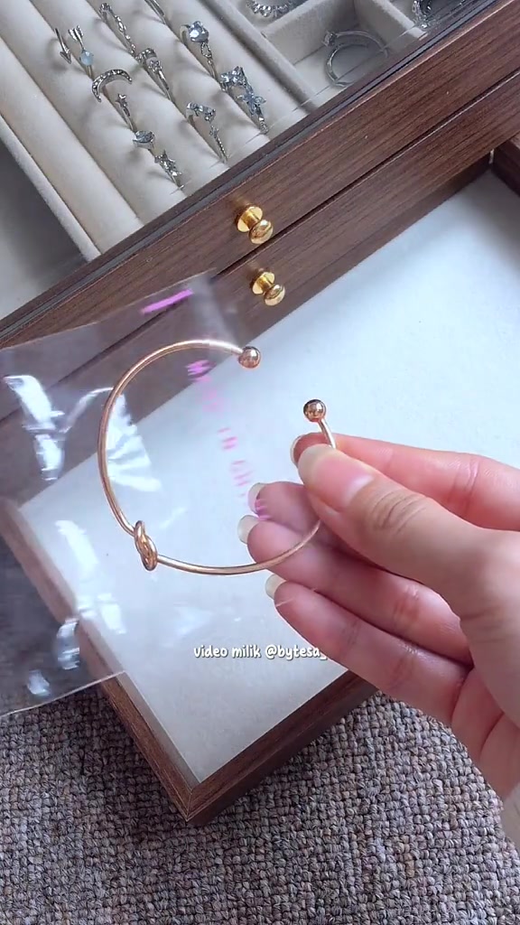 Gelang open cuff rose gold berujung bola kecil dipegang dua jari sehingga celah terbukanya terlihat jelas