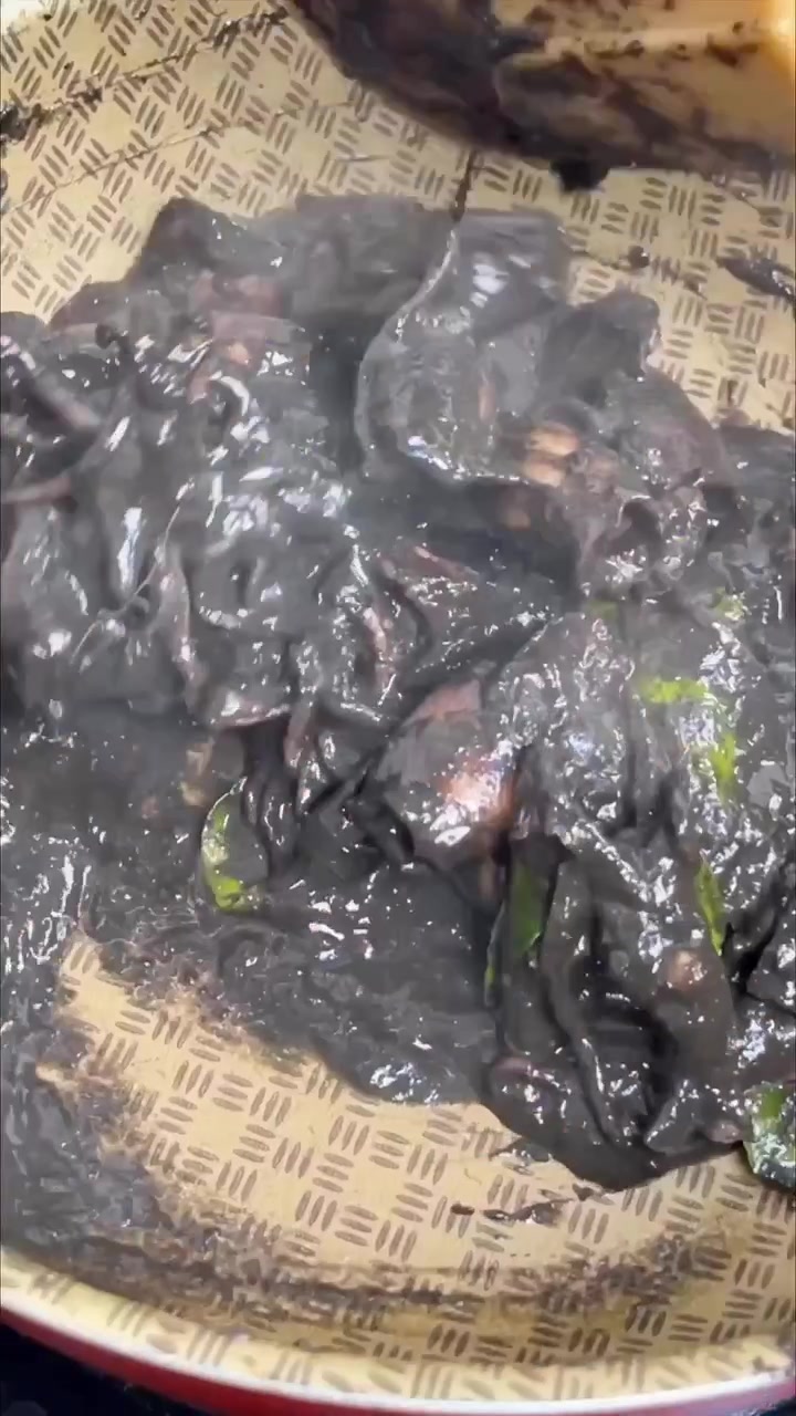 Cumi berbumbu tinta hitam sedang dimasak di wajan bermotif anyaman