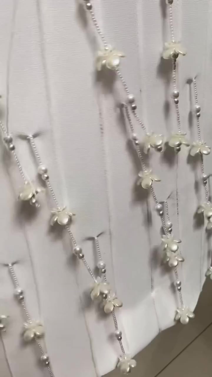 Close-up kain kebaya putih dengan untai manik mutiara dan bunga kecil menjuntai