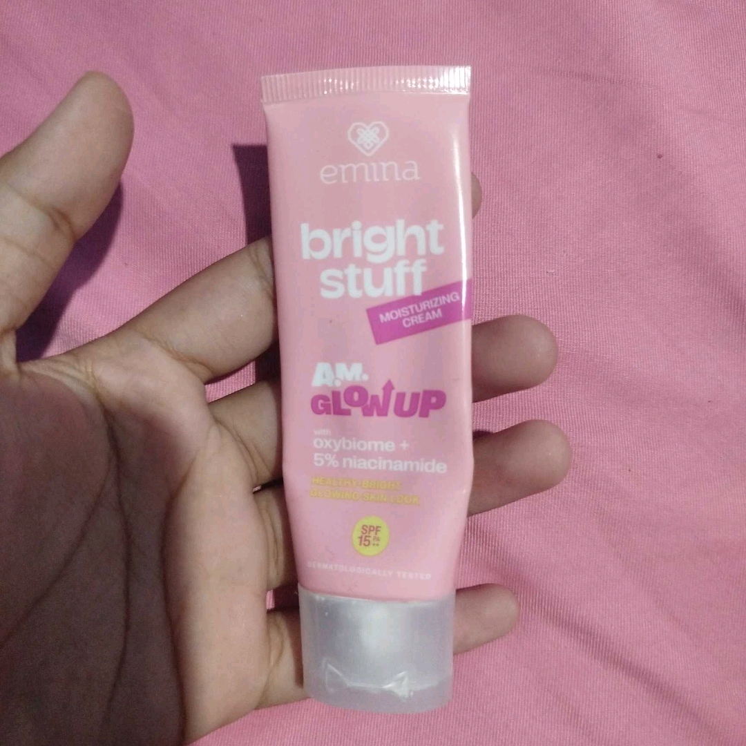 Tube Emina Bright Stuff Moisturizing Cream dipegang di atas latar merah muda