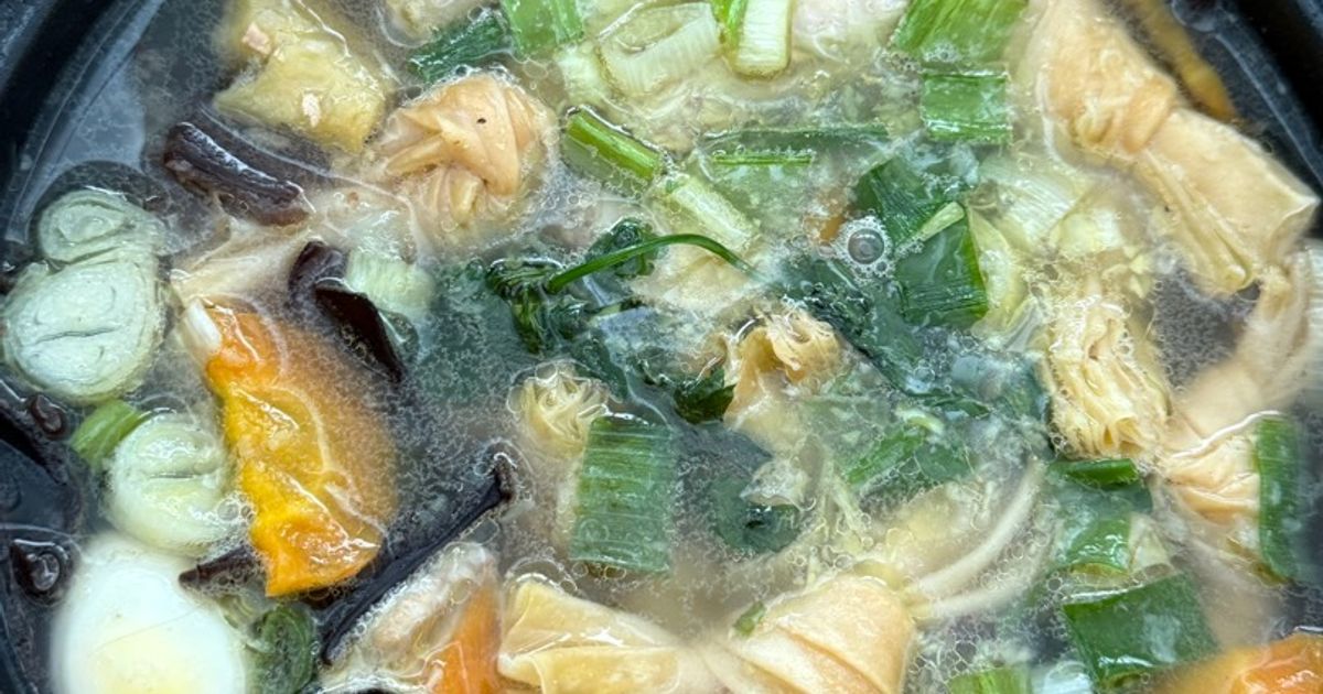 Close-up sup kimlo dengan ayam, wortel, jamur kuping dan sayuran dalam mangkuk gelap