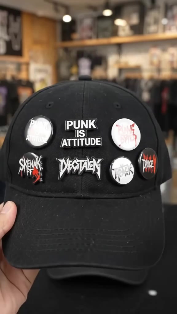 Beberapa pin band terpasang berkelompok pada topi hitam, dengan bentuk bulat dan persegi