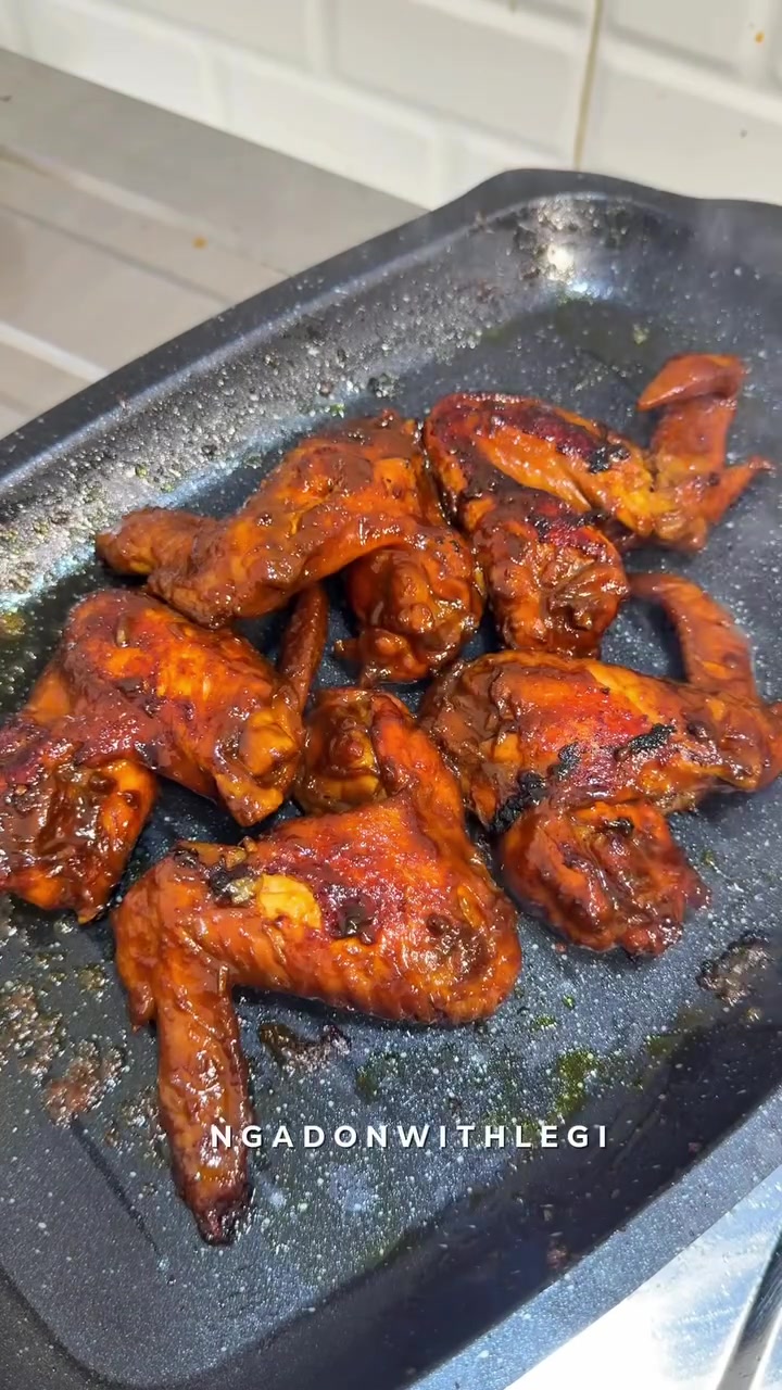 Potongan ayam bakar berbumbu merah mengilap di atas grill pan