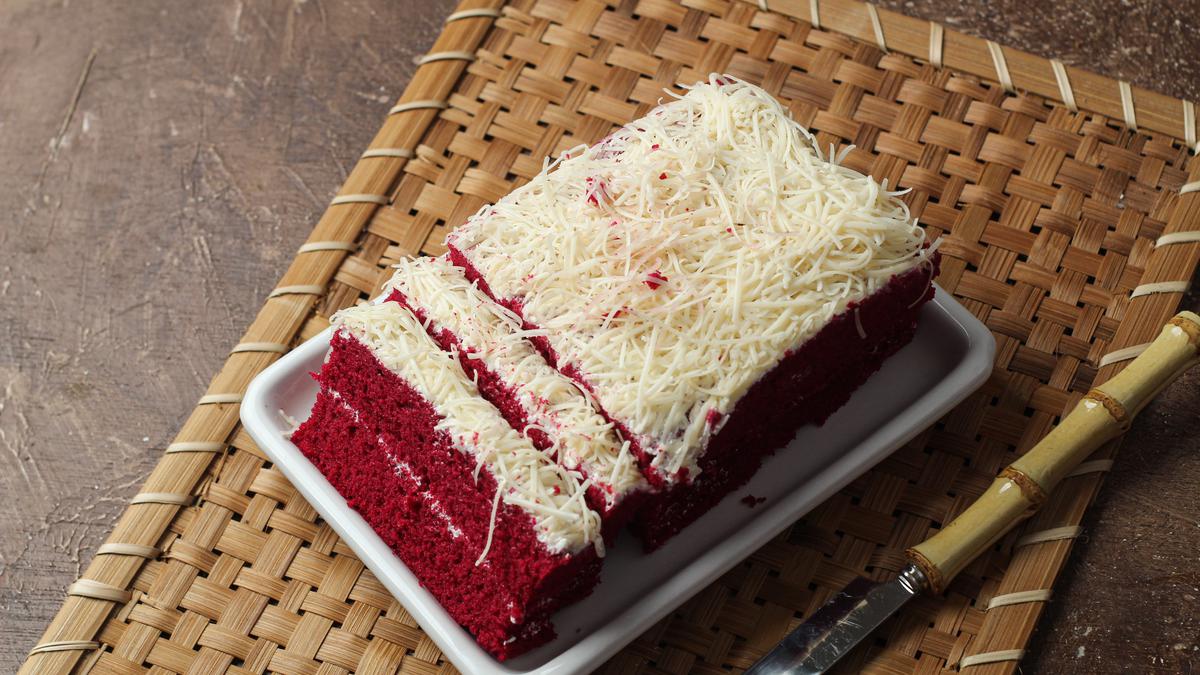 Bolu red velvet dengan lapisan keju parut di atas nampan anyaman