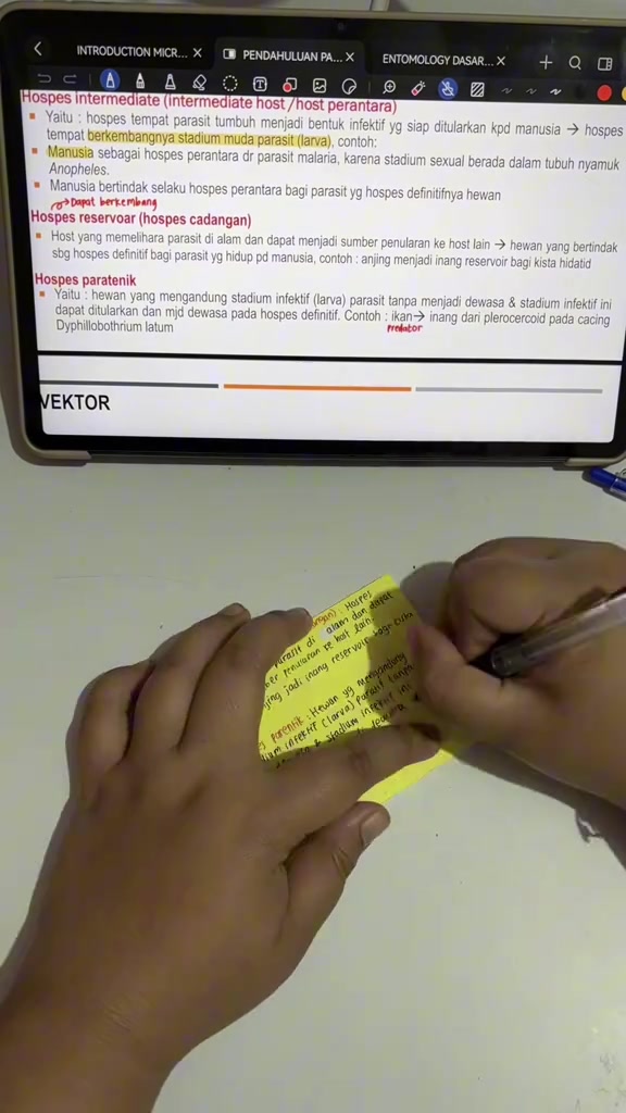 Tangan menulis ringkasan pendek pada sticky note kuning di depan tablet belajar