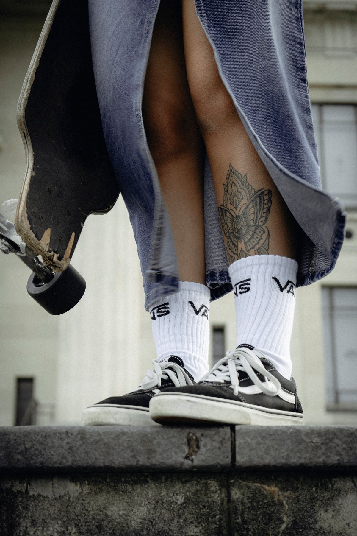 Detail bawahan denim, kaus kaki putih, dan sneakers saat seseorang berdiri di atas skateboard.