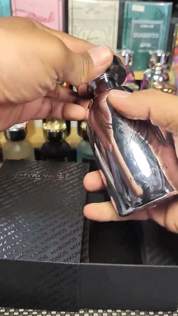 Botol Mykonos berwarna perak dipegang di depan rak parfum