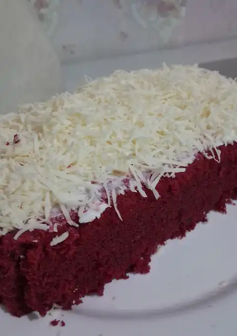 Potongan red velvet kukus berwarna merah dengan lapisan keju parut tebal
