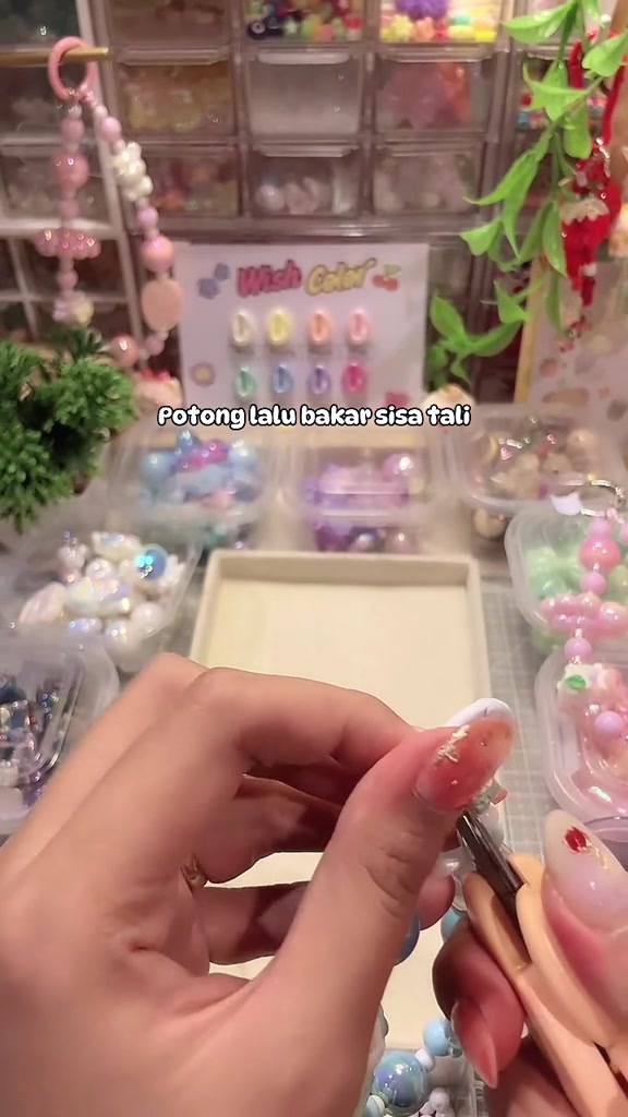 Tangan merapikan ujung tali pada rangkaian phone strap manik di meja kerja