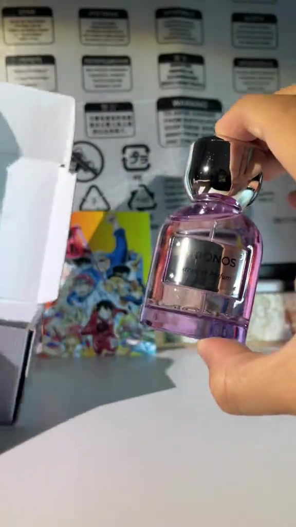 Botol ungu Mykonos Reflection Elixir diangkat di depan kemasan parfum putih