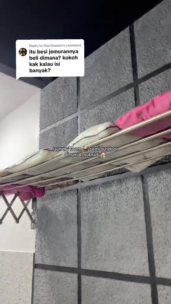 Jemuran lipat terpasang di dinding koridor laundry, dengan pakaian digantung di atas mesin cuci