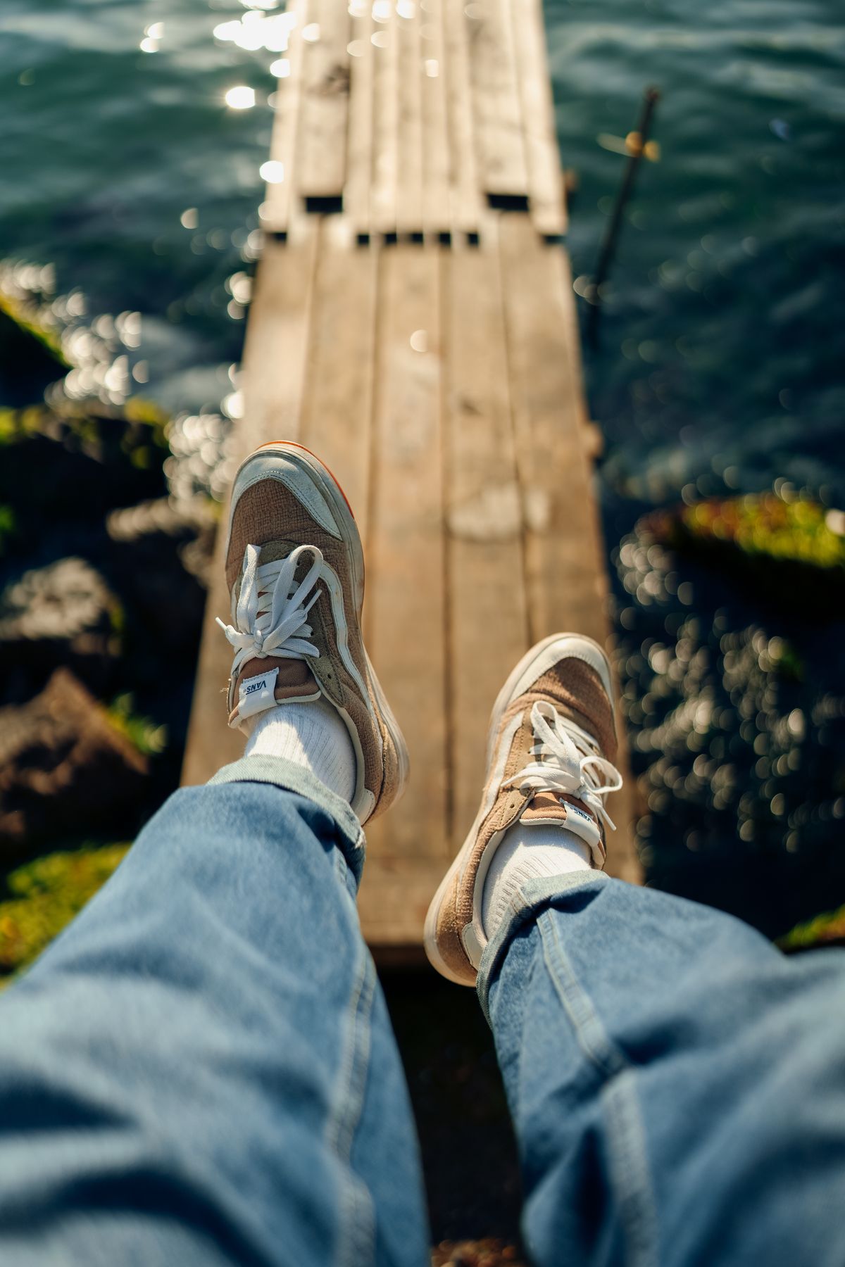 Celana denim dan sneakers berwarna netral terlihat dari sudut pandang pemakainya di dermaga.