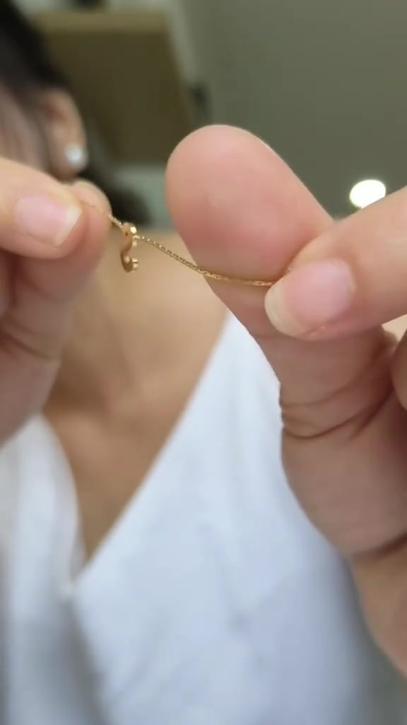 Rantai kalung tipis berwarna emas di antara jari dengan liontin kecil menggantung