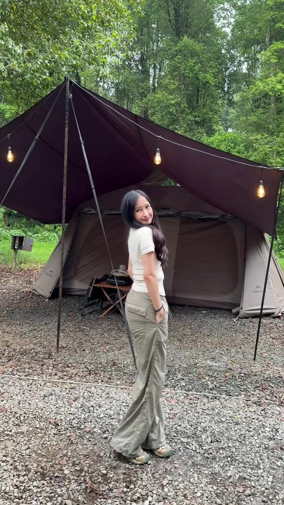 Atasan putih dan celana longgar abu-abu dipakai di area tenda camping