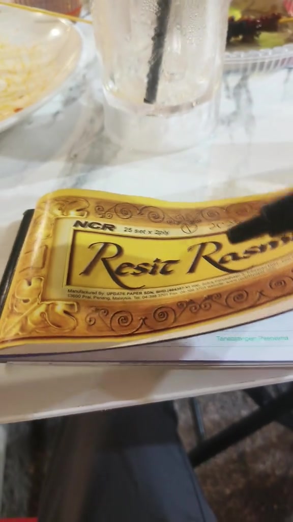 Buku catatan kuning di atas meja dengan gelas minum di latar