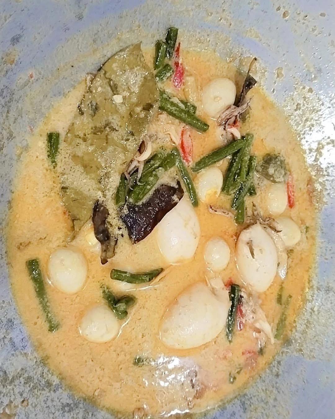 Cumi dan daun aromatik berada di dalam kuah gulai santan dalam panci